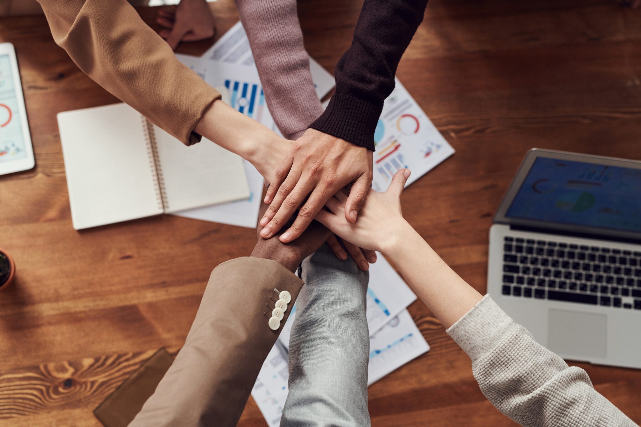 Hands of a diverse team stacked together on a table to represent teamwork and unity.